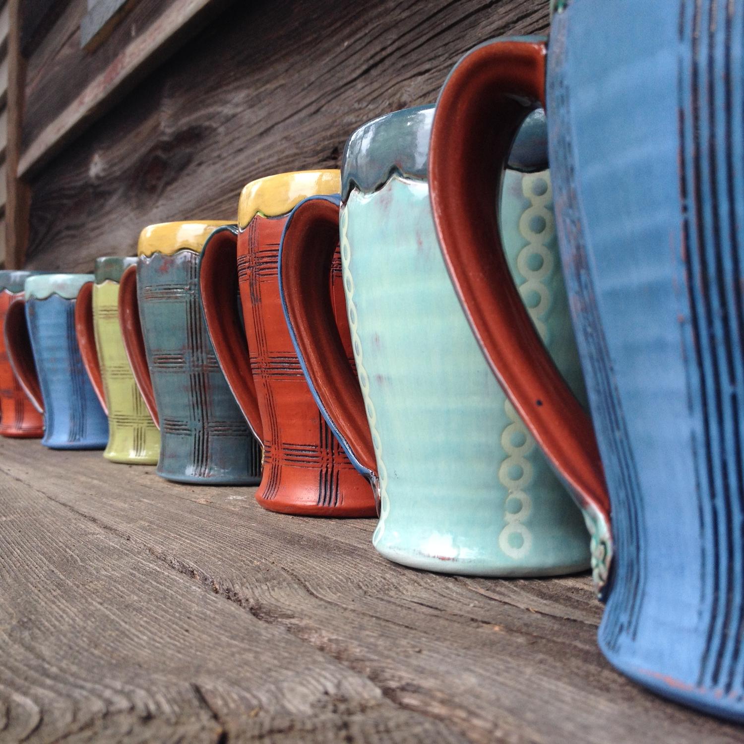 Row of vibrant colored ceramic coffee mugs created by artist Amy Sanders.