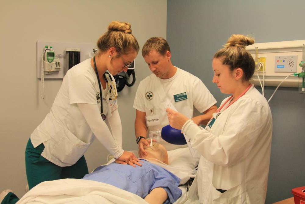 三个学生在健康模拟中心练习心肺复苏术.