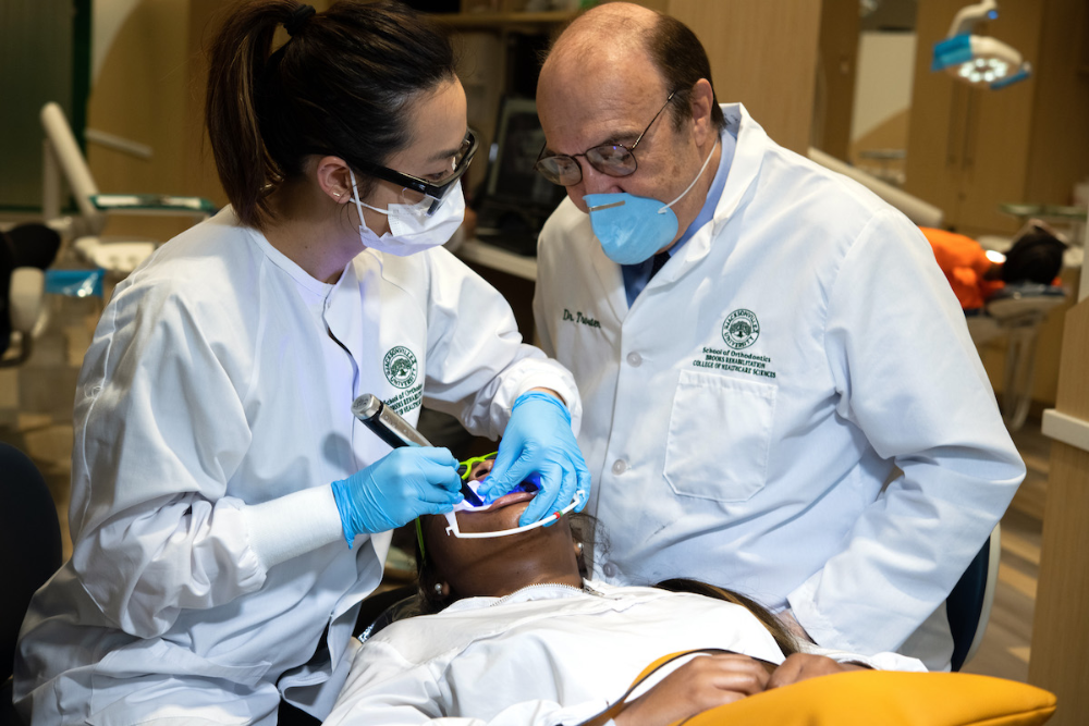 一名学生正在给病人做牙科检查，教授在一旁看着.